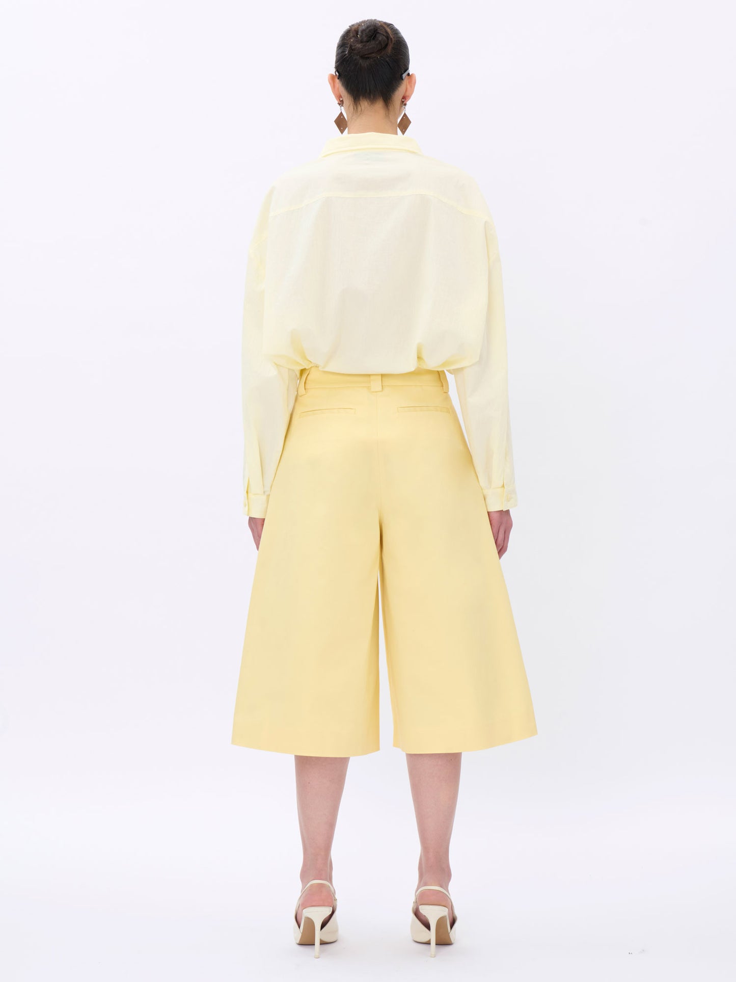 Person wearing a light yellow outfit with wide-leg pants on a white background