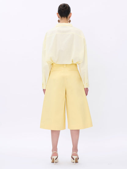 Person wearing a light yellow outfit with wide-leg pants on a white background