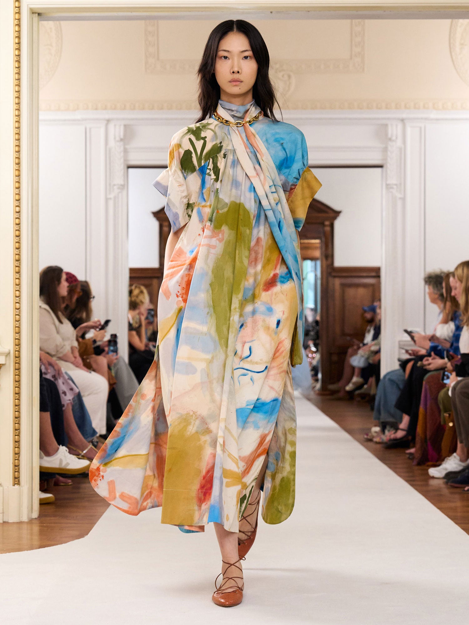 Model walking on a runway wearing a colorful dress with abstract patterns.