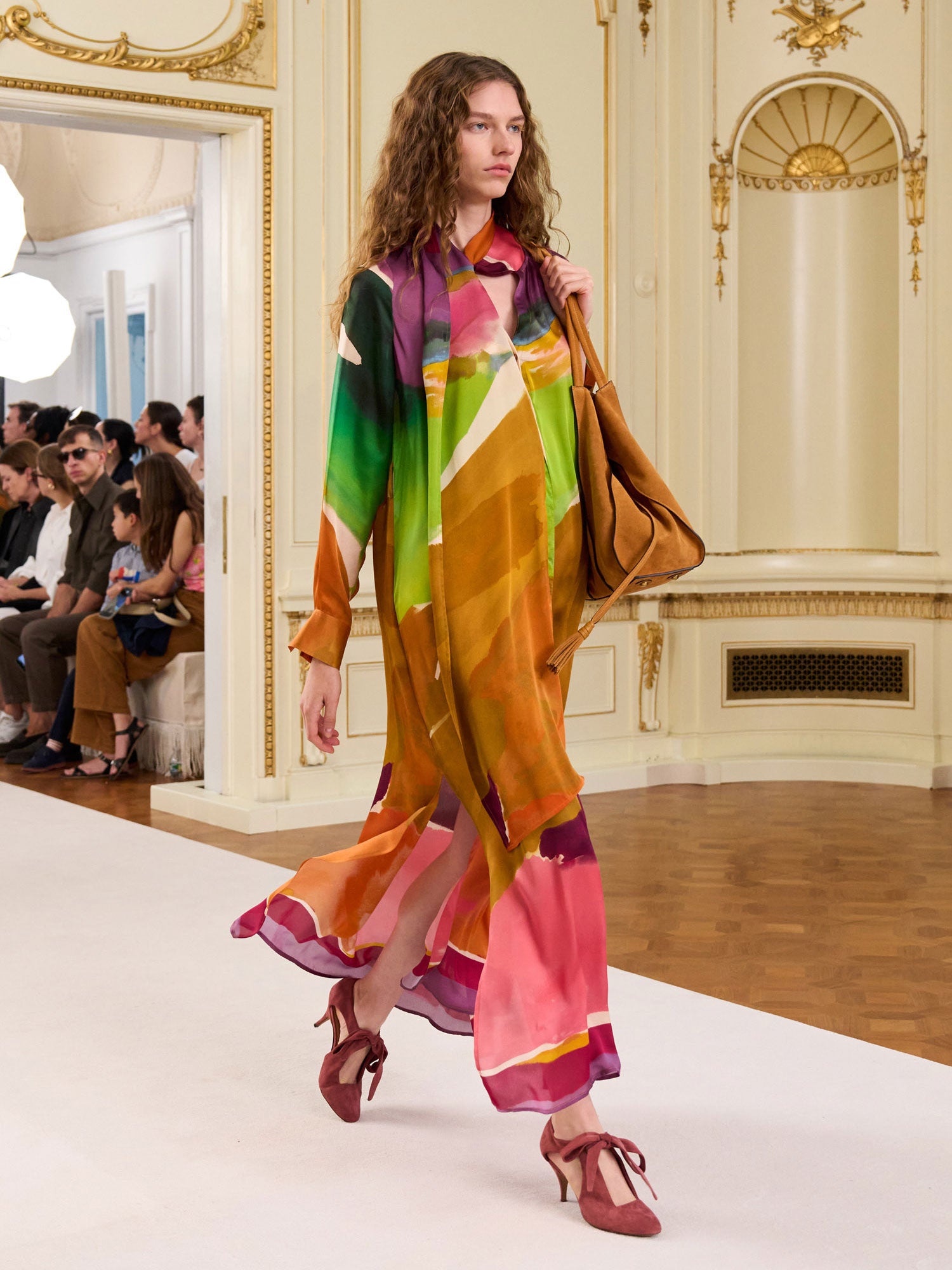 Model wearing a colorful dress with a patterned bag in an indoor setting.