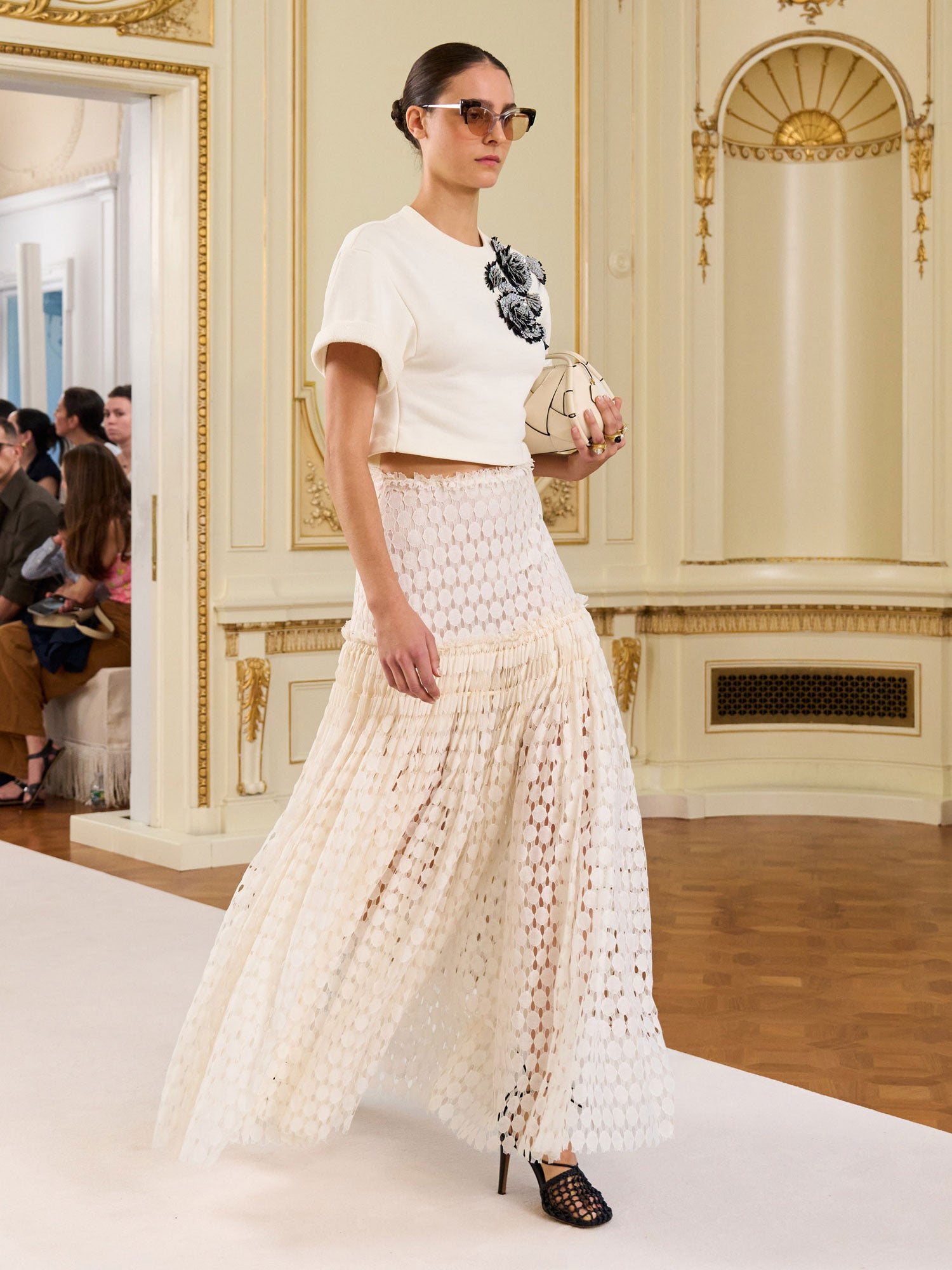 Woman in a stylish outfit with a white top and patterned skirt in an elegant interior setting.