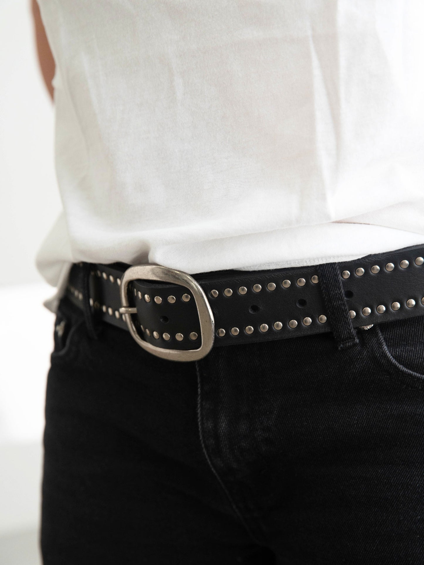 Person wearing a black belt with a silver buckle on a plain background
