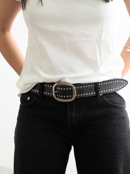 Person wearing a white shirt and black pants with a studded belt.