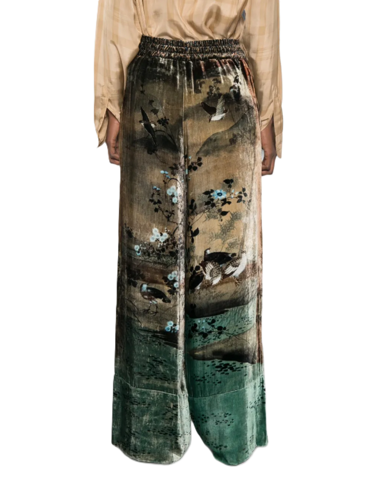 A model is wearing wide-leg trousers featuring a vintage-style landscape print with birds, trees, and a green-teal gradient at the bottom, paired with a beige top against a plain white background.