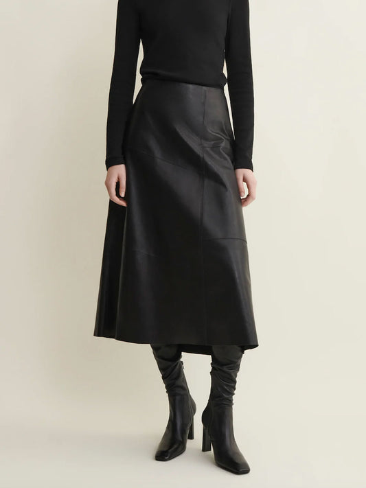 Person wearing a black leather skirt and black boots on a beige background