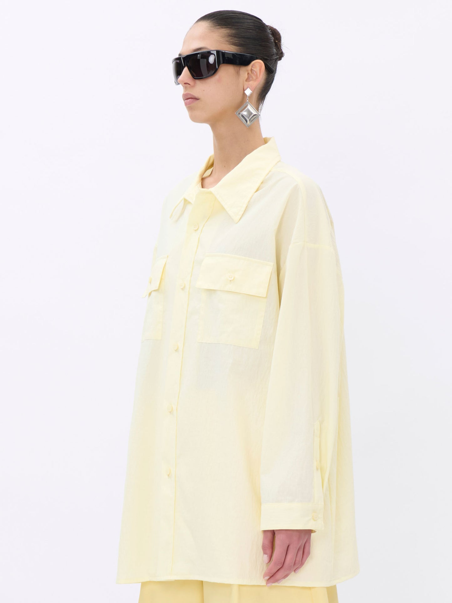 Woman wearing a light yellow shirt and sunglasses on a white background