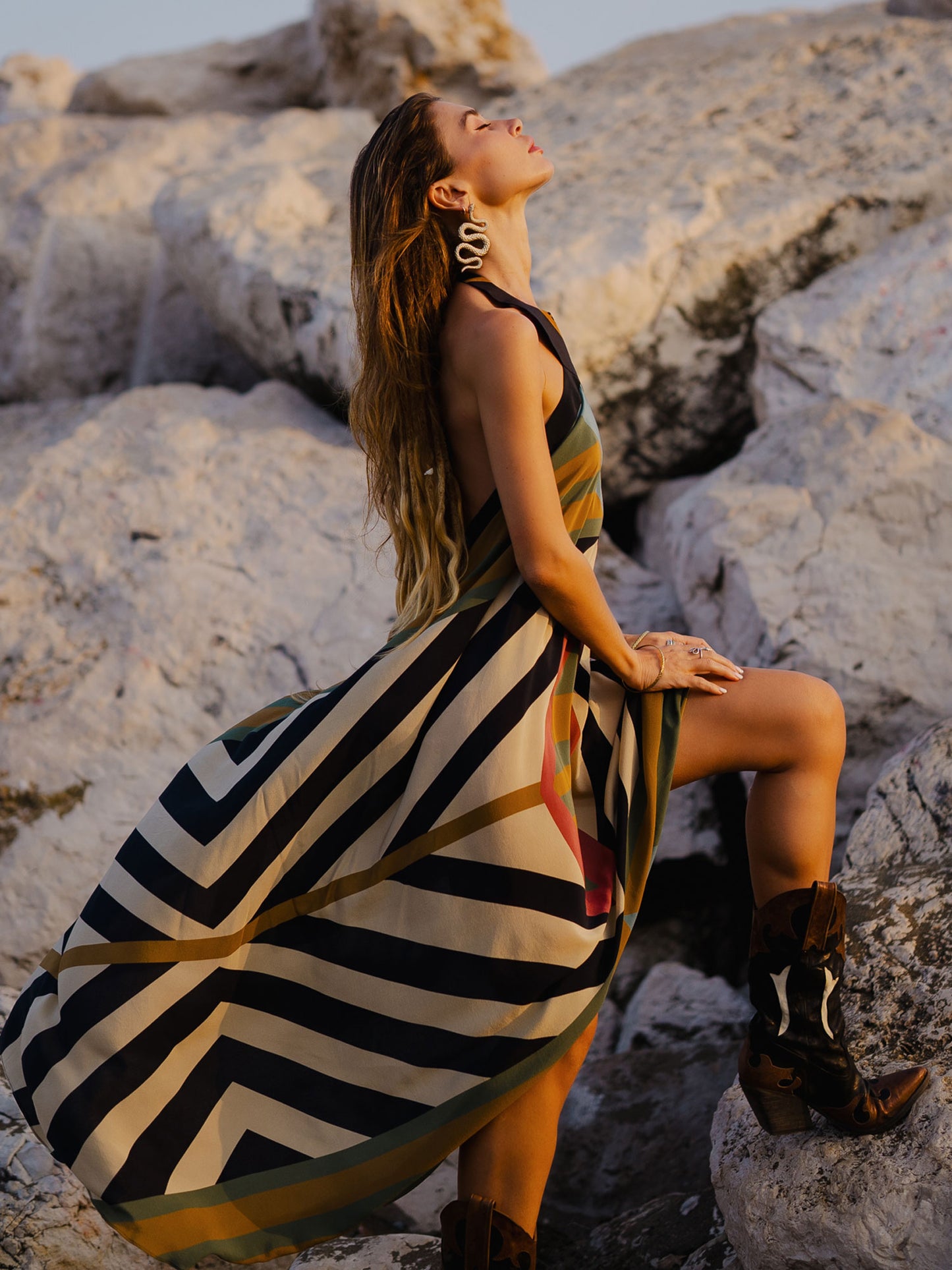 Woman in a striped dress sitting on rocks with a scenic background